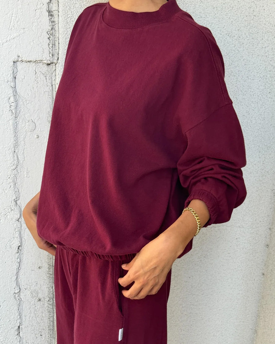 side view of model wearing cabernet colored long sleeve mock neck top with elastic hem