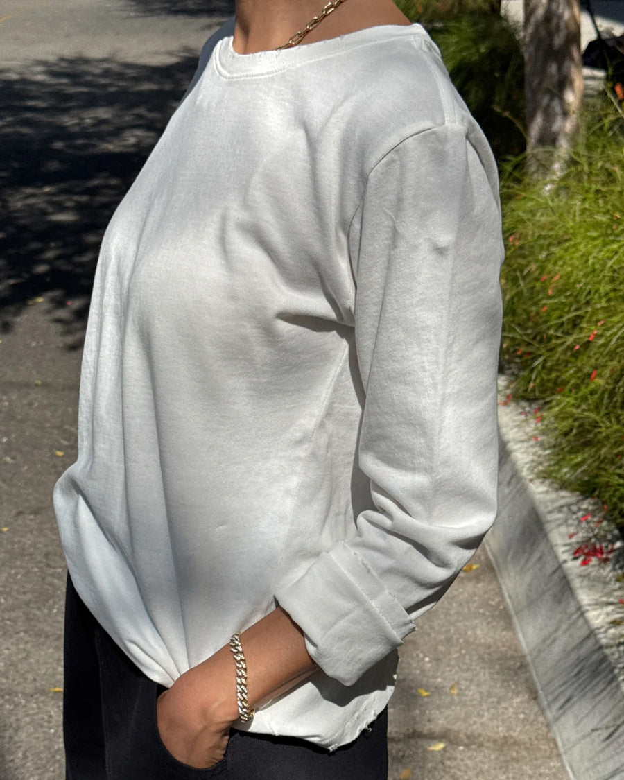 side view of model wearing relaxed fit white long sleeve top with slight distressing around the collar