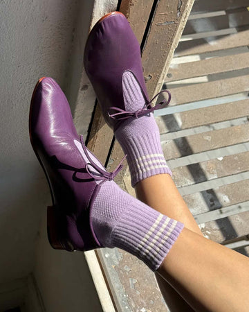 model wearing light purple socks with three white stripes and dark purple shoes