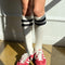 model wearing white knee high socks with two black stripes on the top and red sneakers