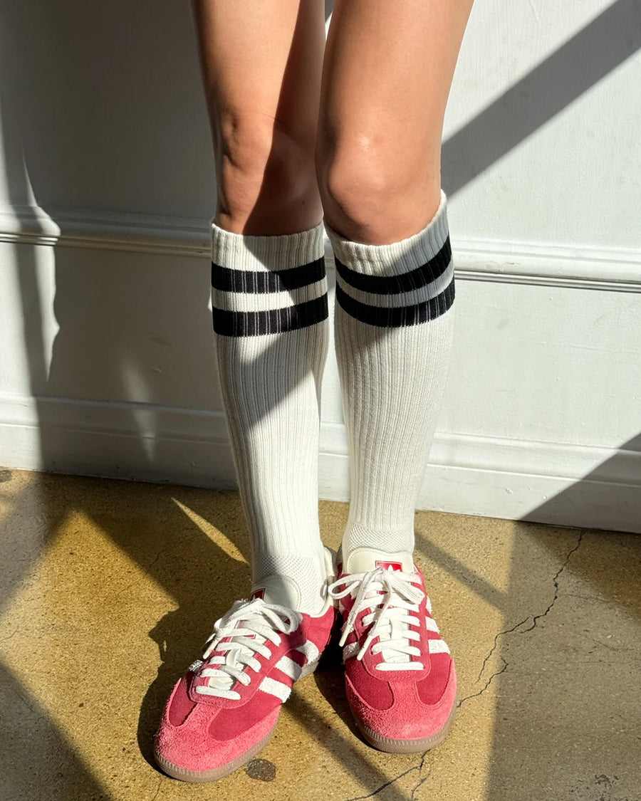 model wearing white knee high socks with two black stripes on the top and red sneakers