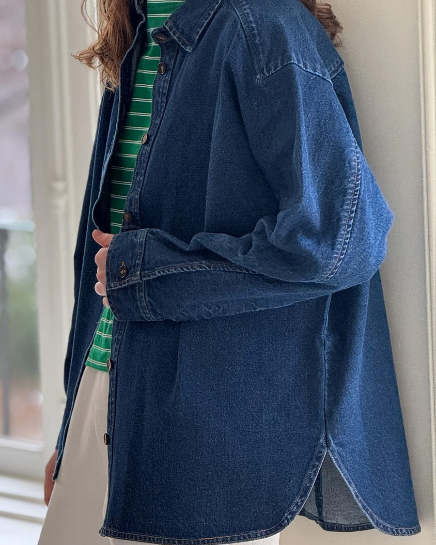 side view of model wearing oversized dark denim button down shirt with striped tee and white pants