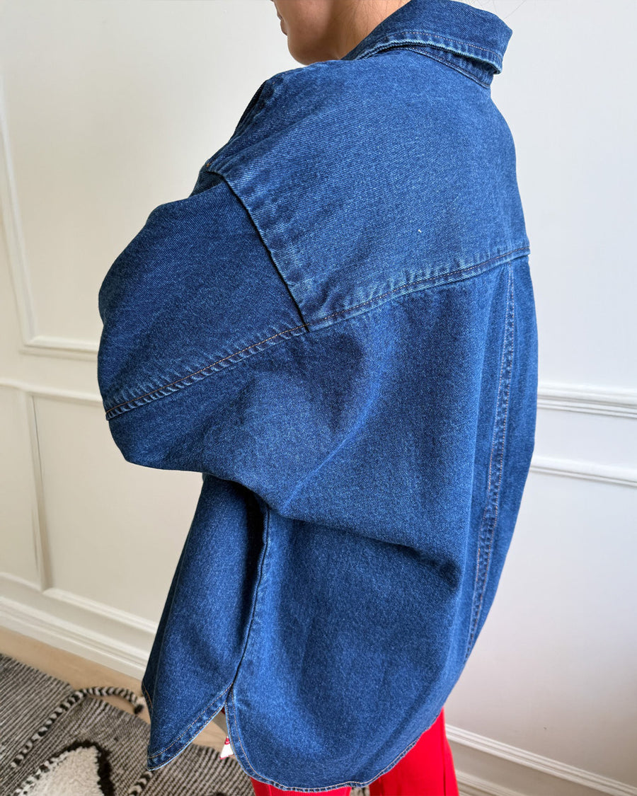 back view of model wearing oversized dark denim button down shirt with striped tee and white pants