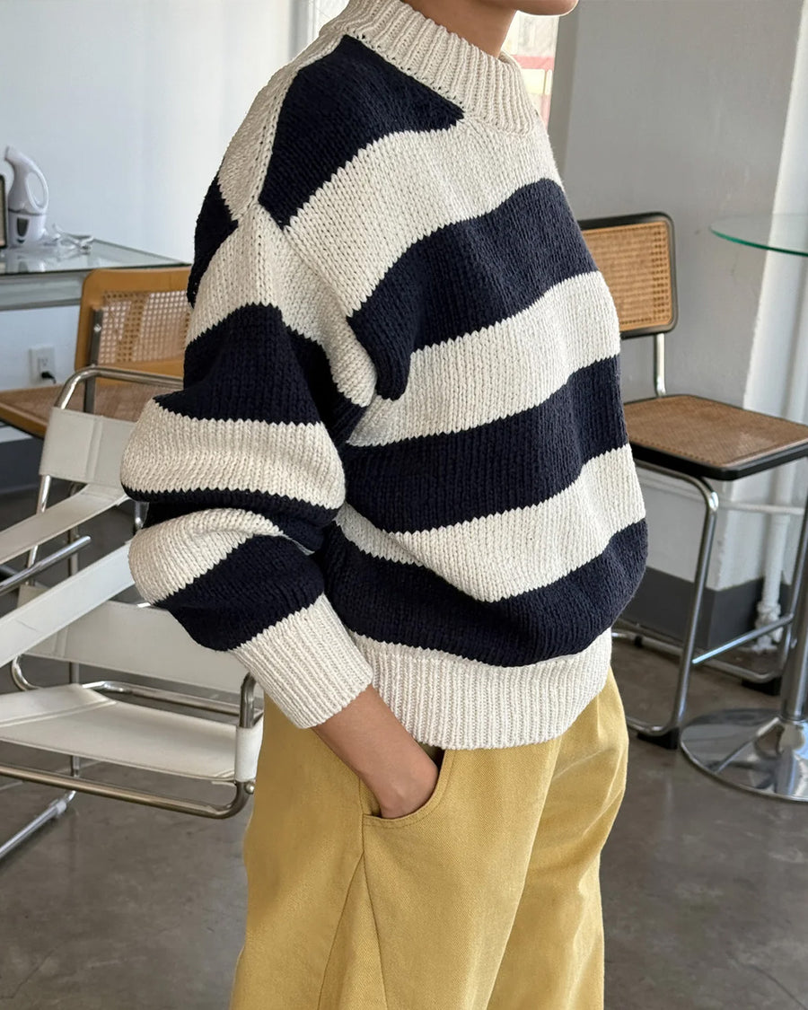 side view of model wearing navy and white thick stripe sweater with mock neckline with yellow bottoms