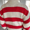 back view of model wearing red and white thick stripe sweater with mock neckline with denim bottoms