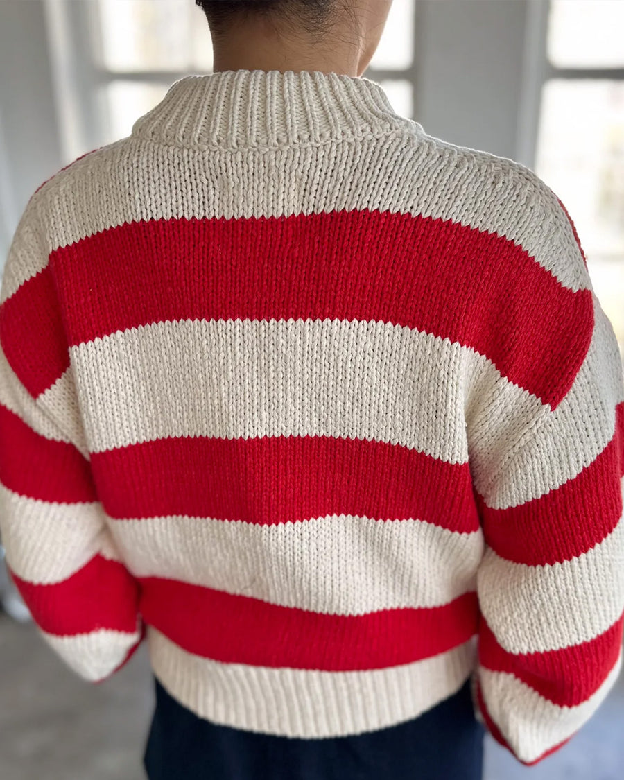 back view of model wearing red and white thick stripe sweater with mock neckline with denim bottoms