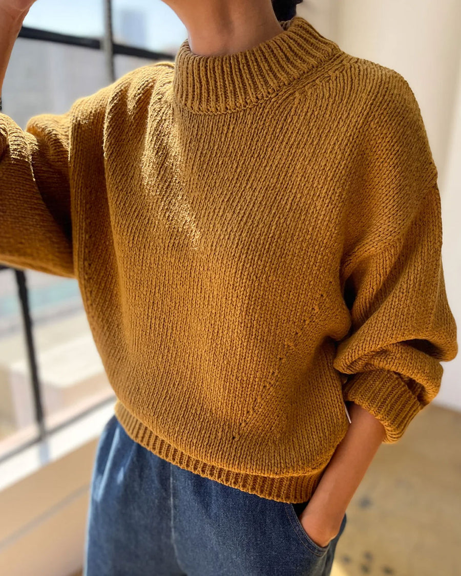 side view of model wearing mustard yellow cotton sweater with thick banded bottom and mockneck