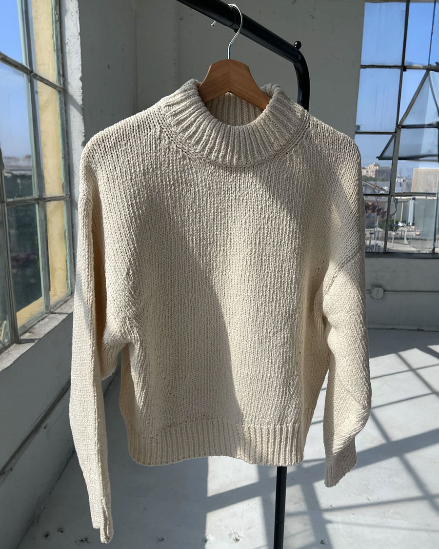 model wearing cream cotton sweater with thick banded bottom and mockneck on a hanger