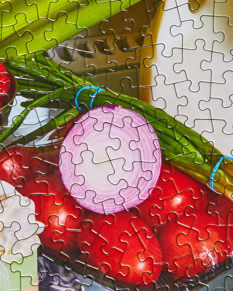 up close of puzzle pieces of le puzz 1000 piece puzzle with a fridge filled with very delicious food and snacks