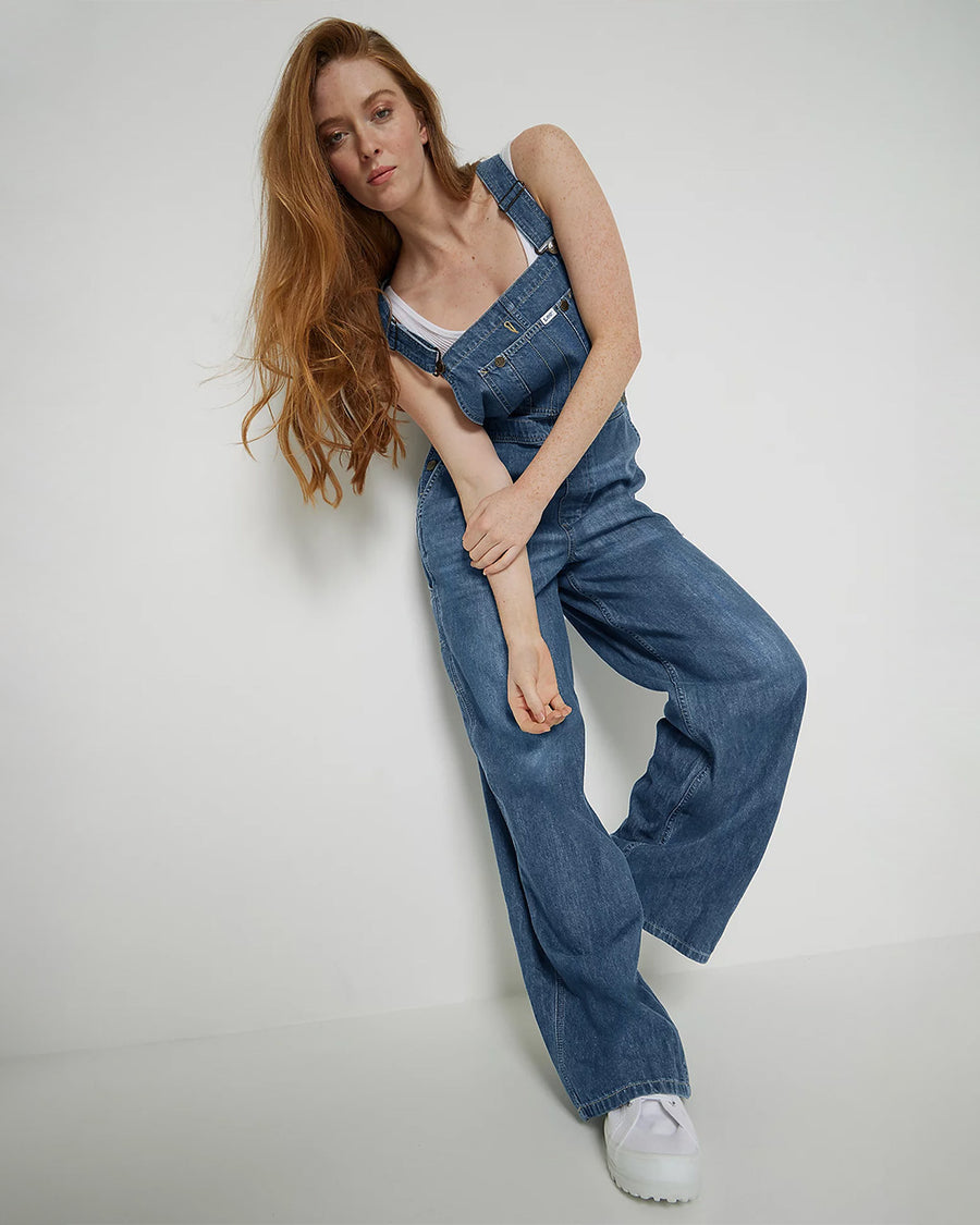 model wearing medium denim overalls with front pocket and lee tag