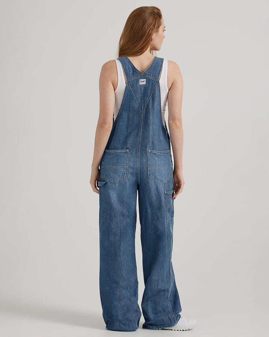 back view of model wearing medium denim overalls with front pocket and lee tag