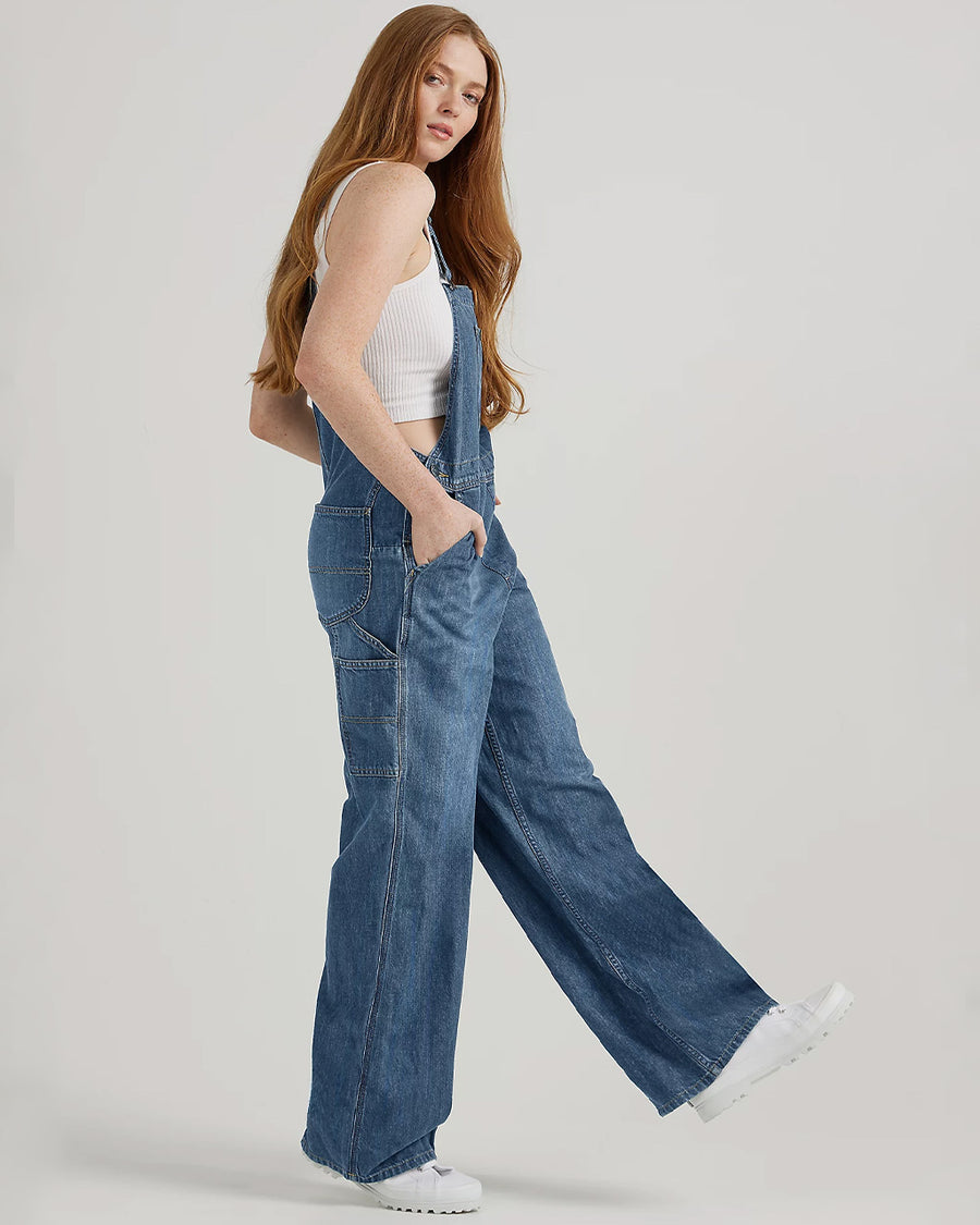 side view of model wearing medium denim overalls with front pocket and lee tag