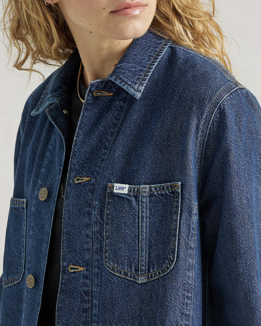 up close of model wearing medium denim chore coat with four front patch pockets and button front