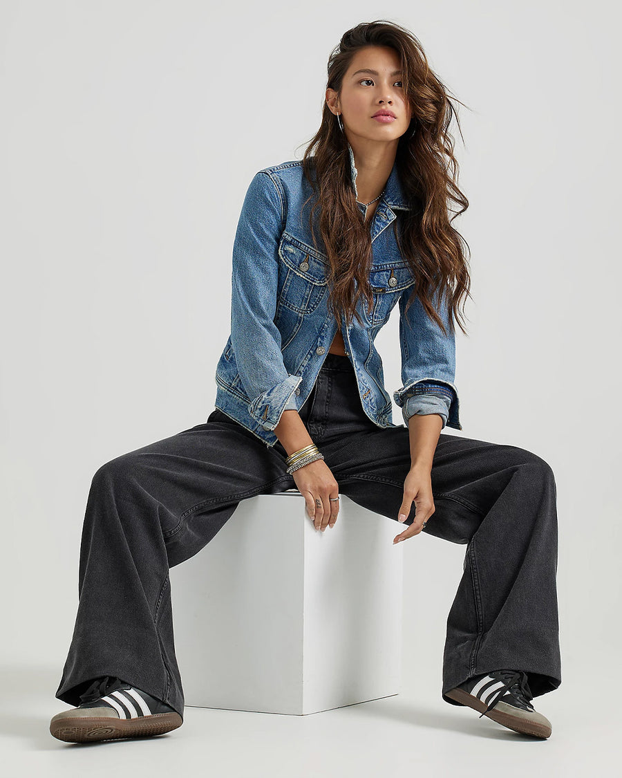 model sitting on white block while wearing black denim a-line trouser