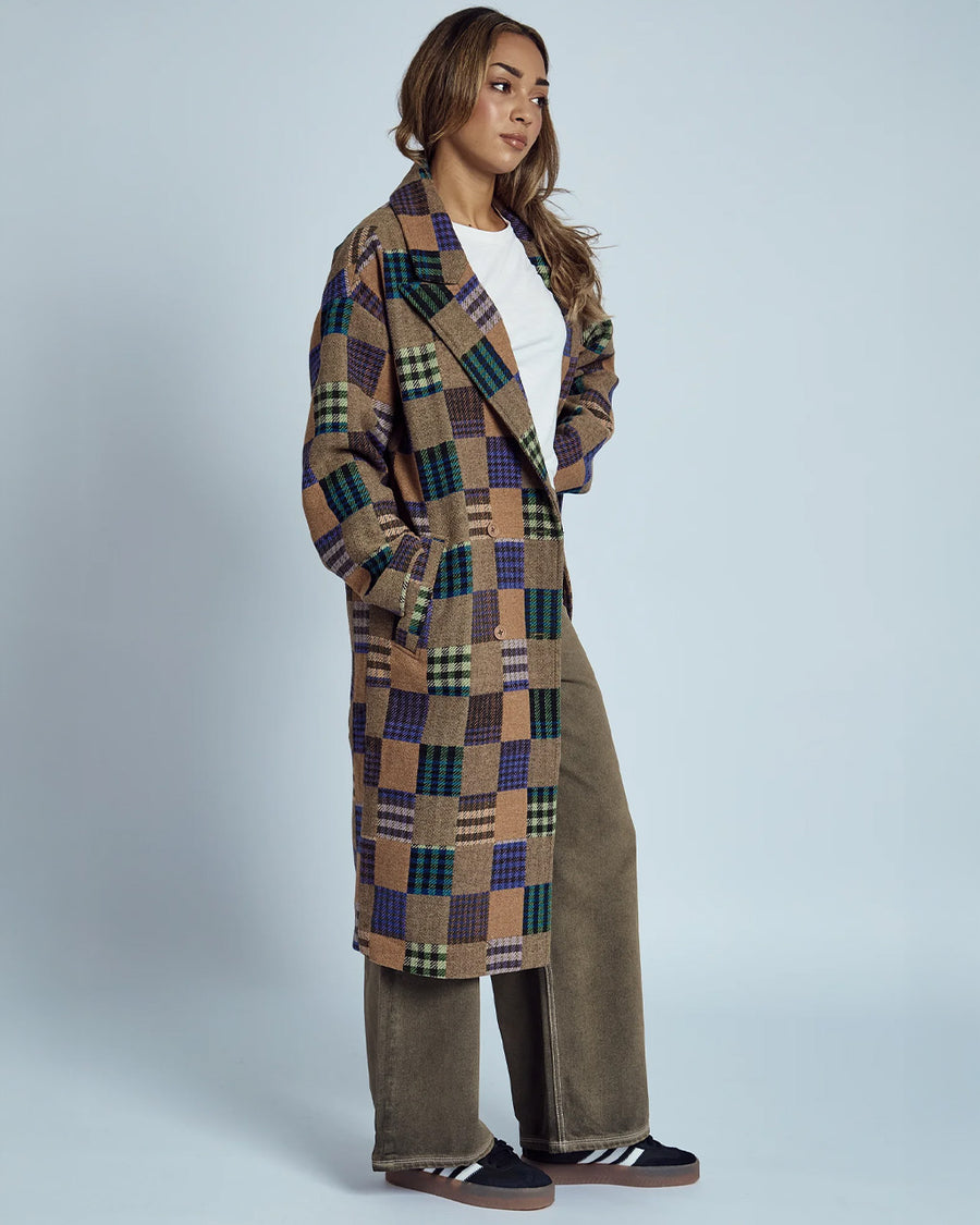 side view of model wearing brown mid length coat with front lapel, button front and colorful checkered patches