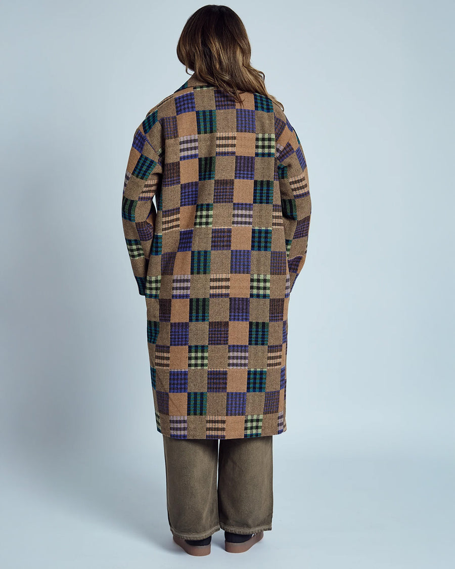 back view of model wearing brown mid length coat with front lapel, button front and colorful checkered patches