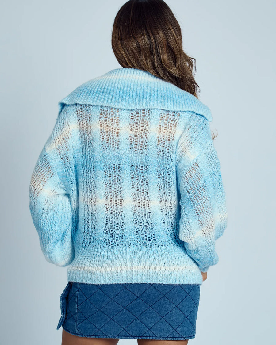 back view of model wearing blue and white knit cardigan with crochet white flower button front and wide lapel collar