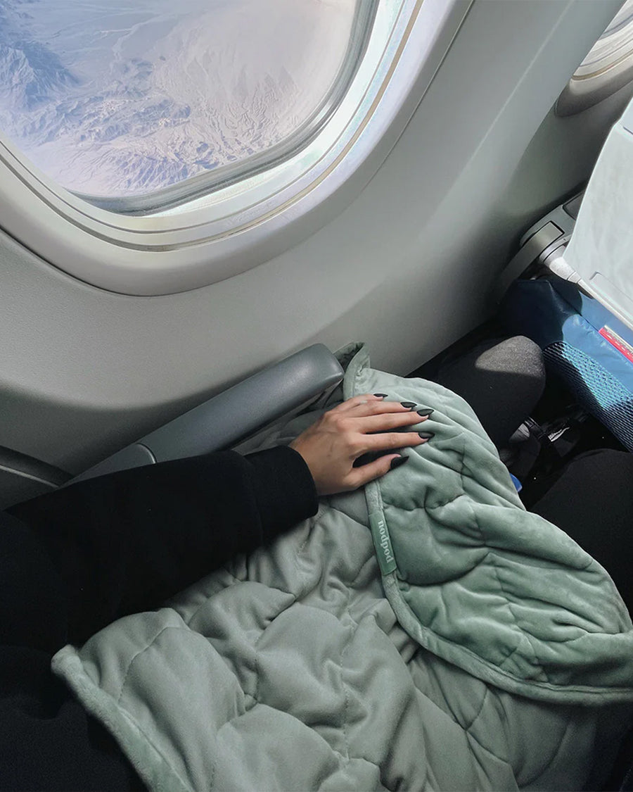 model wearing sage weighted body blanket on their lap on a plane