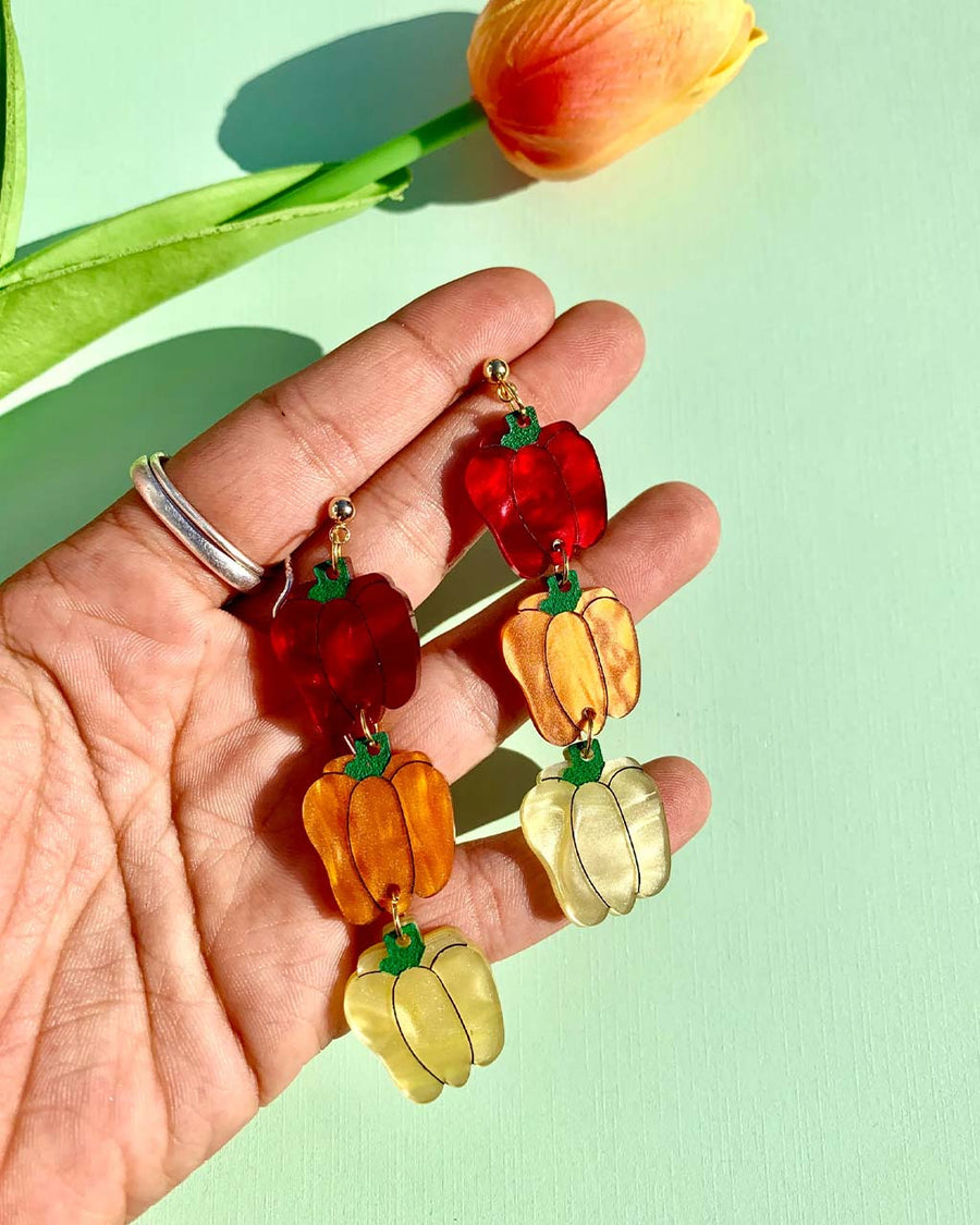 model holding pair of bell pepper earrings in red, orange and yellow tiered