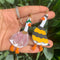 model holding pair of two mismatched duck earrings: goose in a flower costume and goose in a bee costume