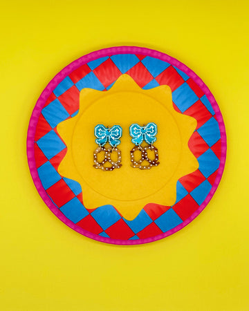 earrings with blue bow stud and pretzel dangle on colorful plate