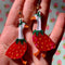 model holding large dangle earrings with geese dressed as a strawberry