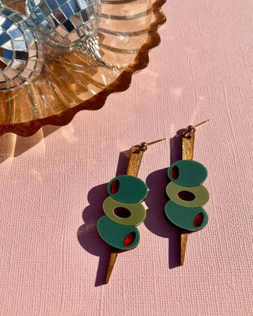 pair of earrings with three green olives with a wooden stick through them