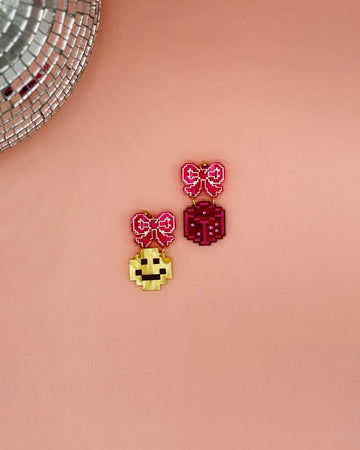 earrings with pink bow stud and one earring with a yellow smiley dangle and a pink dice dangle