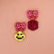 earrings with pink bow stud and one earring with a yellow smiley dangle and a pink dice dangle