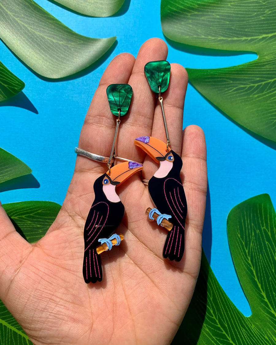 model holding toucan shaped dangle earrings with green leaf stud