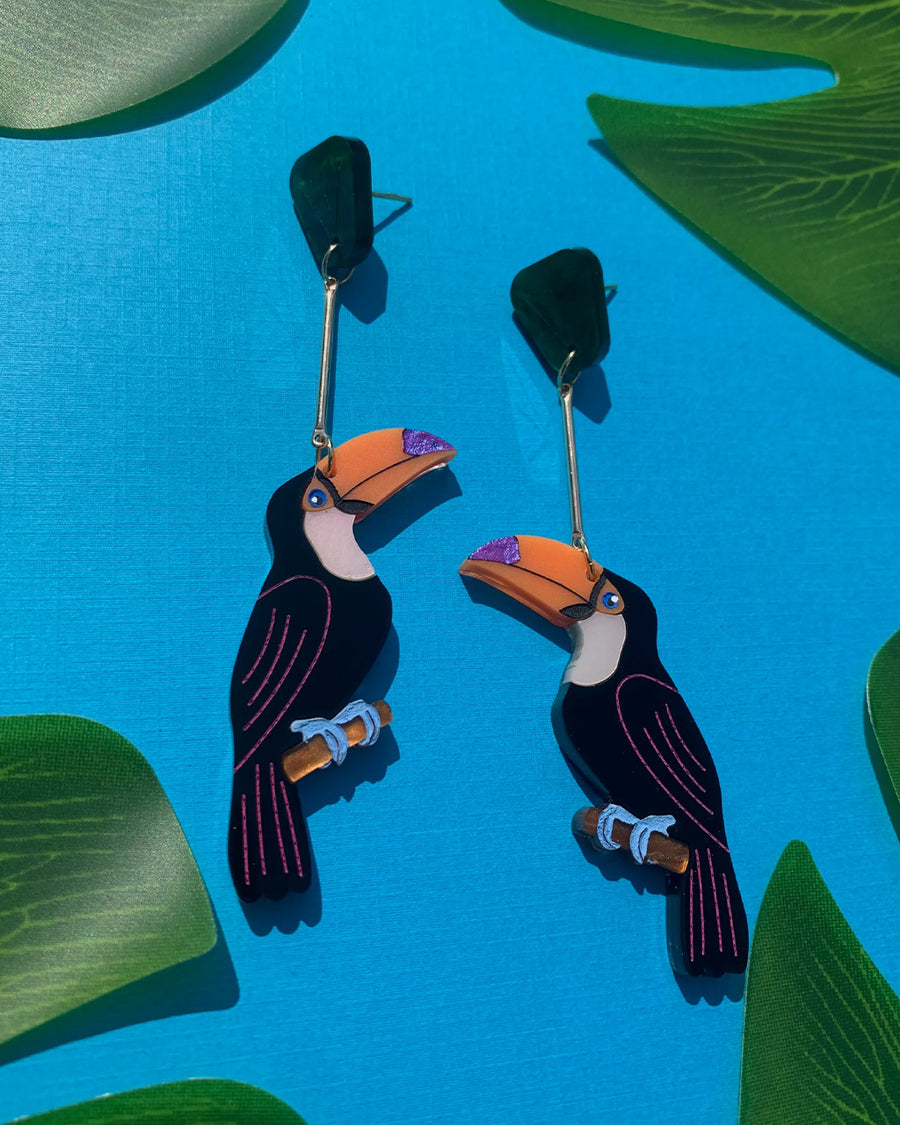 toucan shaped dangle earrings with green leaf stud on a blue background