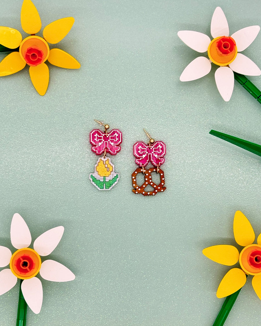 earrings with pink bow stud and one earring with a yellow tulip and one with a pretzel dangle