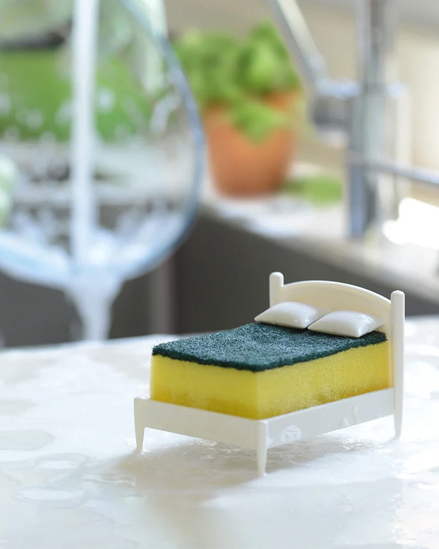 white mini bed frame with green and yellow kitchen sponge on it by a sink