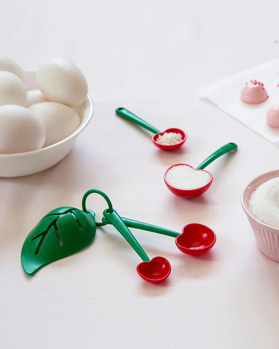 cherry shaped measuring spoons with various baking ingredients in them