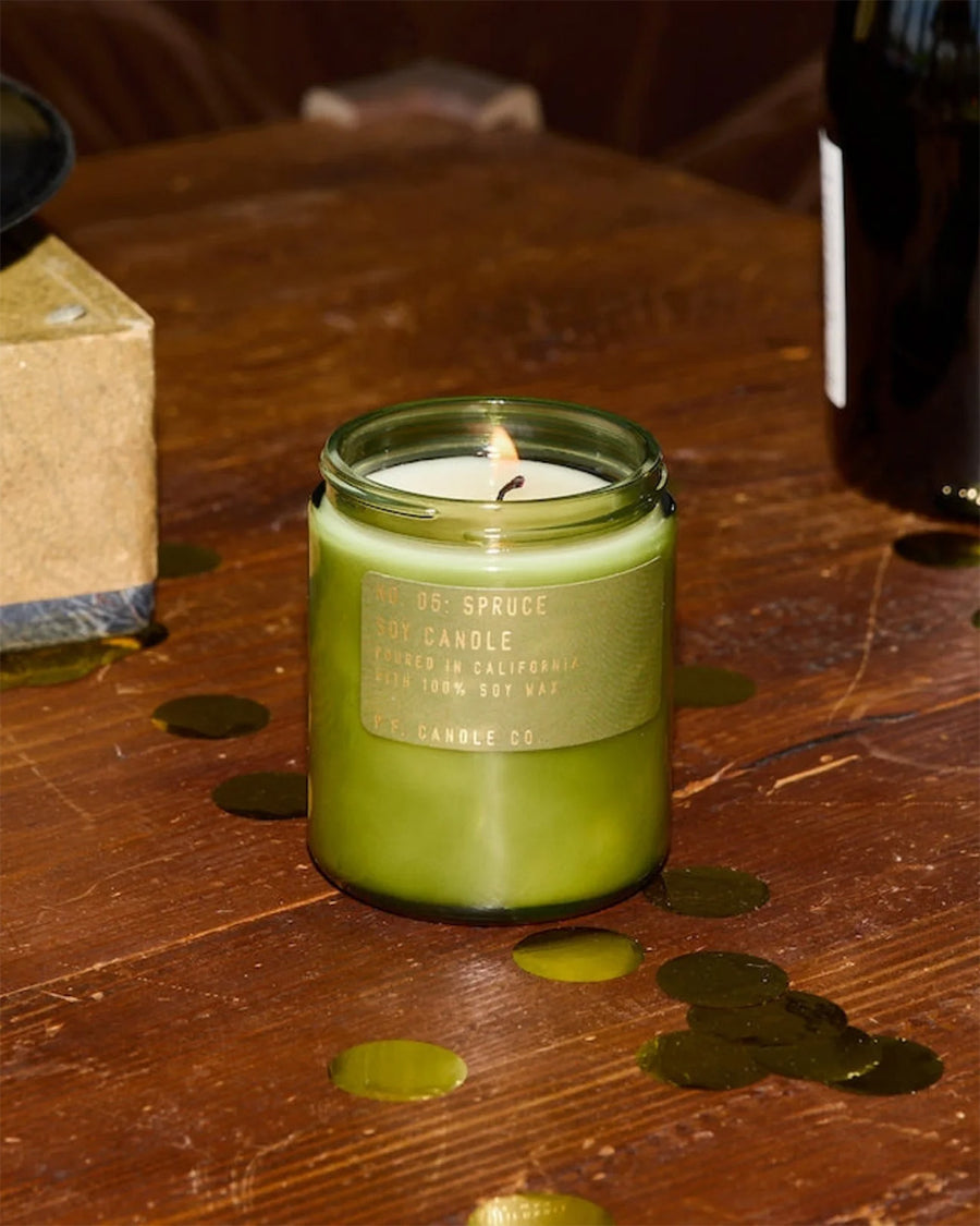 spruce scented soy standard candle on a table surrounded by gold confetti