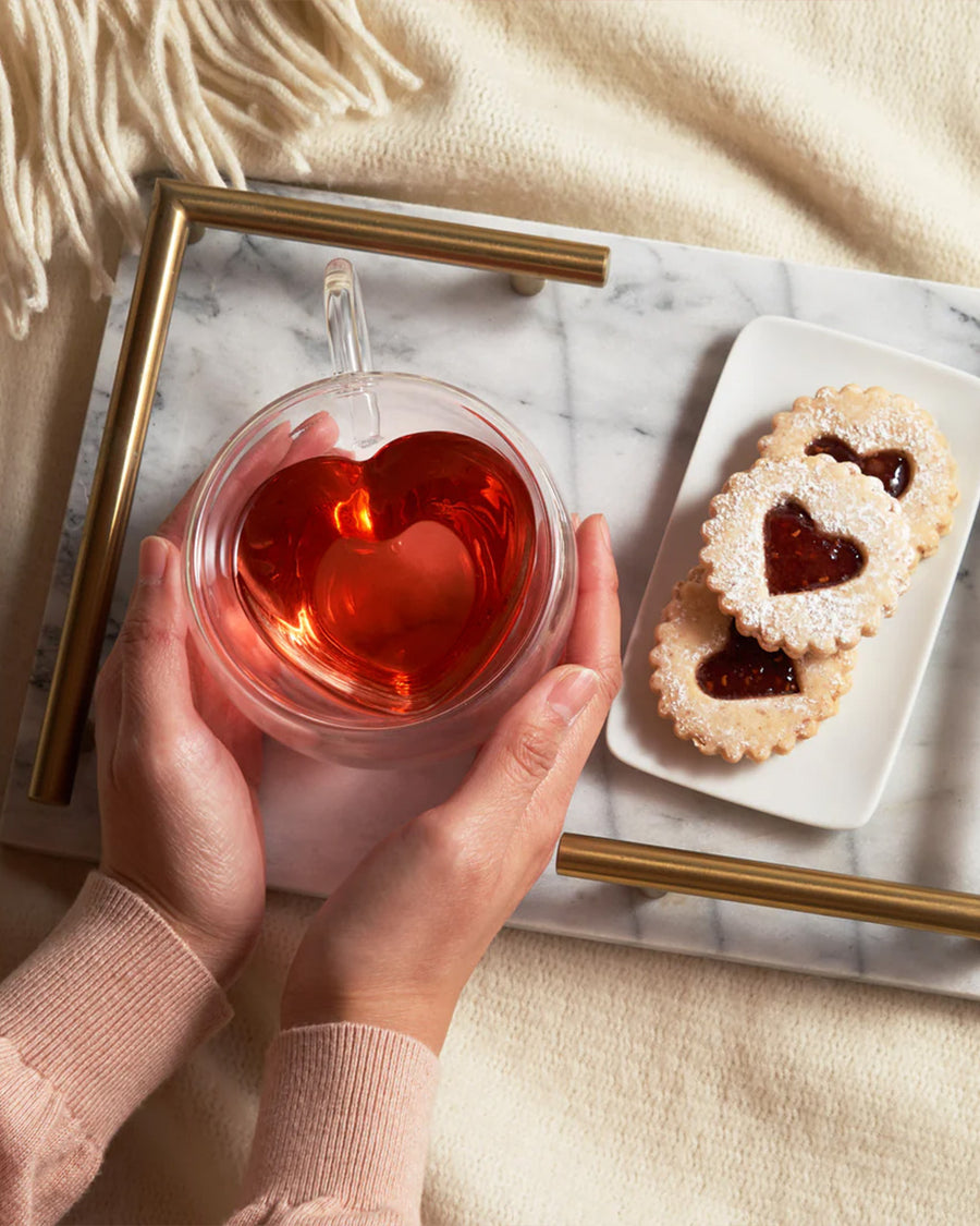 model holding heart shaped clear glass mug with red tea inside on a table display with red tea inside