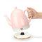 model lifting pink ceramic electric tea kettle off of rose gold base