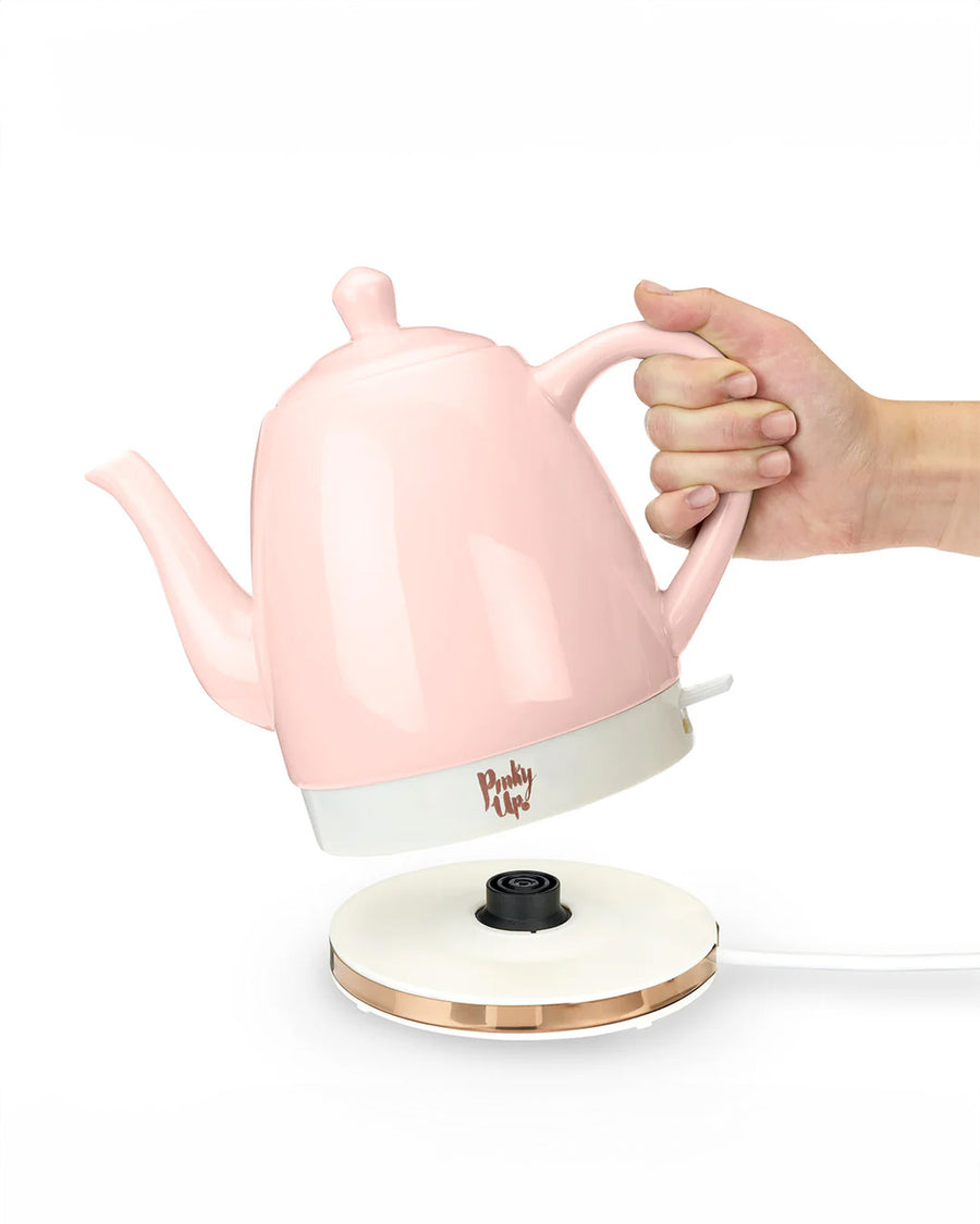 model lifting pink ceramic electric tea kettle off of rose gold base