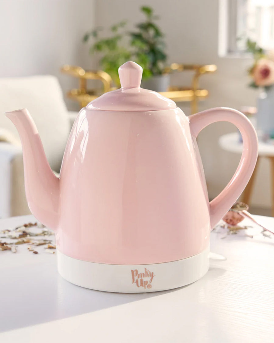 pink ceramic electric tea kettle off of rose gold base on a table