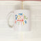 white ceramic mug with colorful 'the book was better' across the front in a book