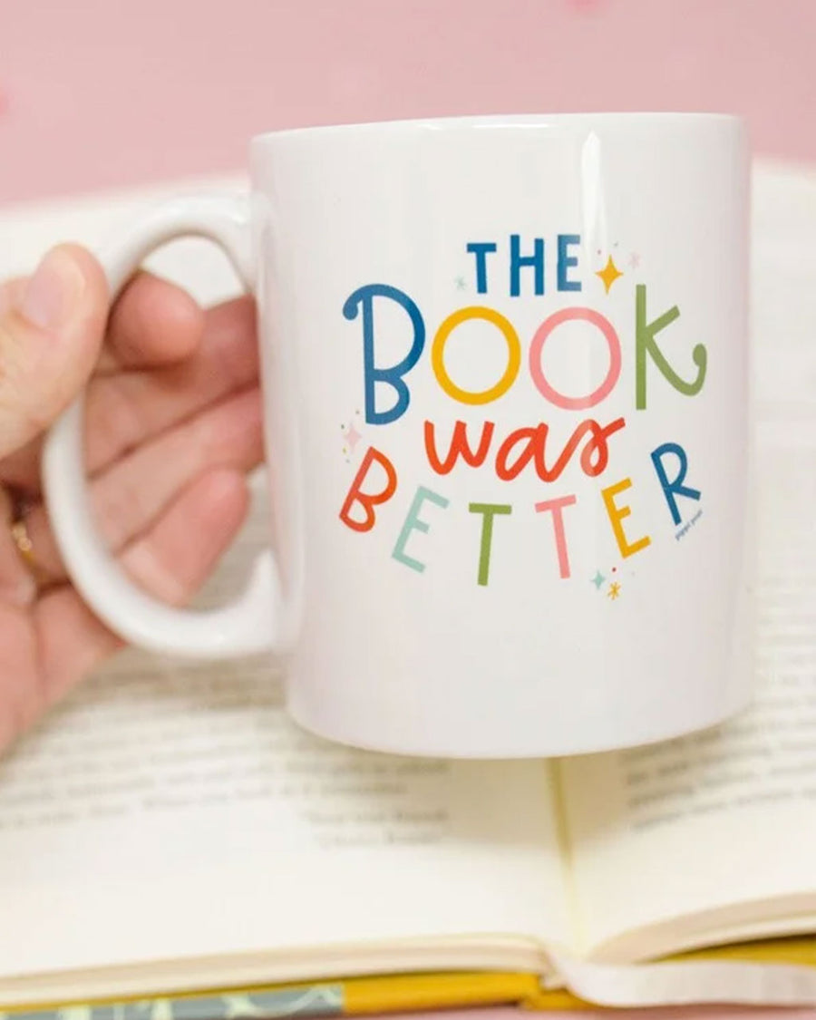 model holding white ceramic mug with colorful 'the book was better' across the front