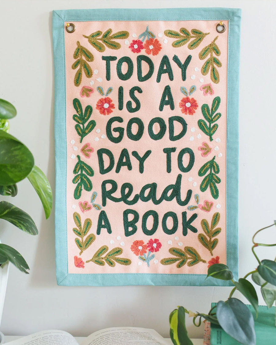 11 in. x 14 in. embroidered wall hanging with colorful flowers and'today is a good day to read a book' across the front displayed on a wall