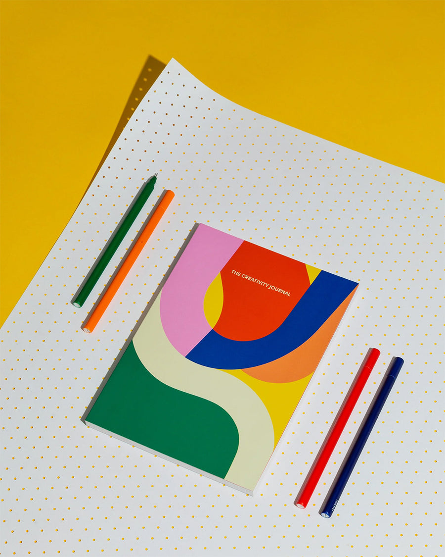 journal with "The Creativity Journal" printed in gold and covered in colorful waves on a yellow background