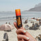 model holding lemon and orange scented lip balm in front of beach background