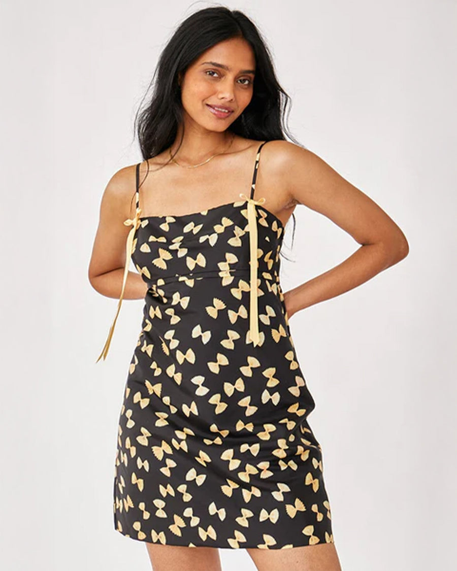 model wearing black mini dress with yellow bow tie pasta print and yellow ribbon on the straps