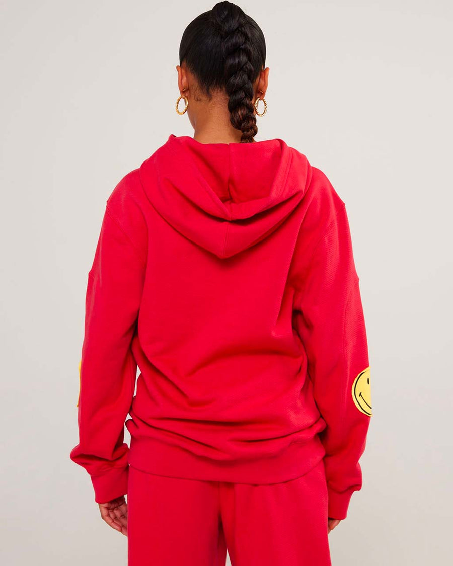 back view of model wearing red hoodie with yellow smiley print on sleeves