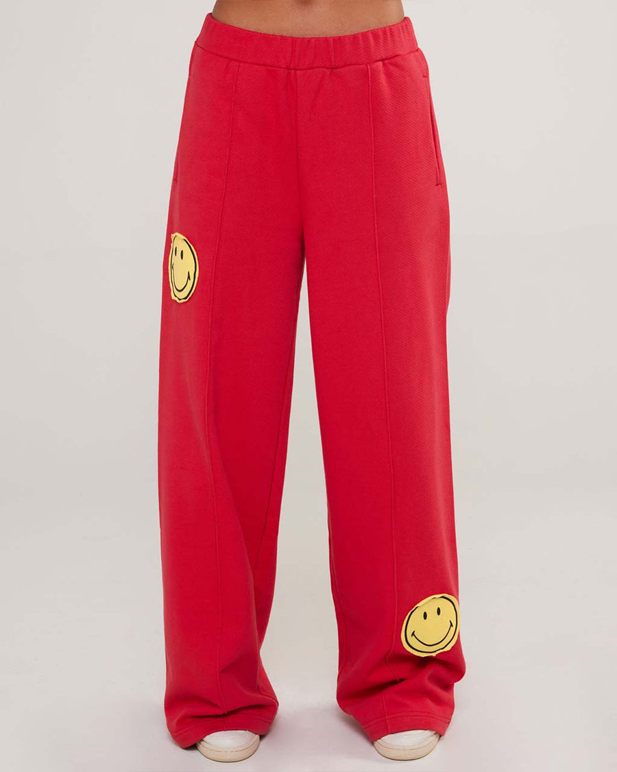 model wearing red sweatpants with yellow smiley print on legs