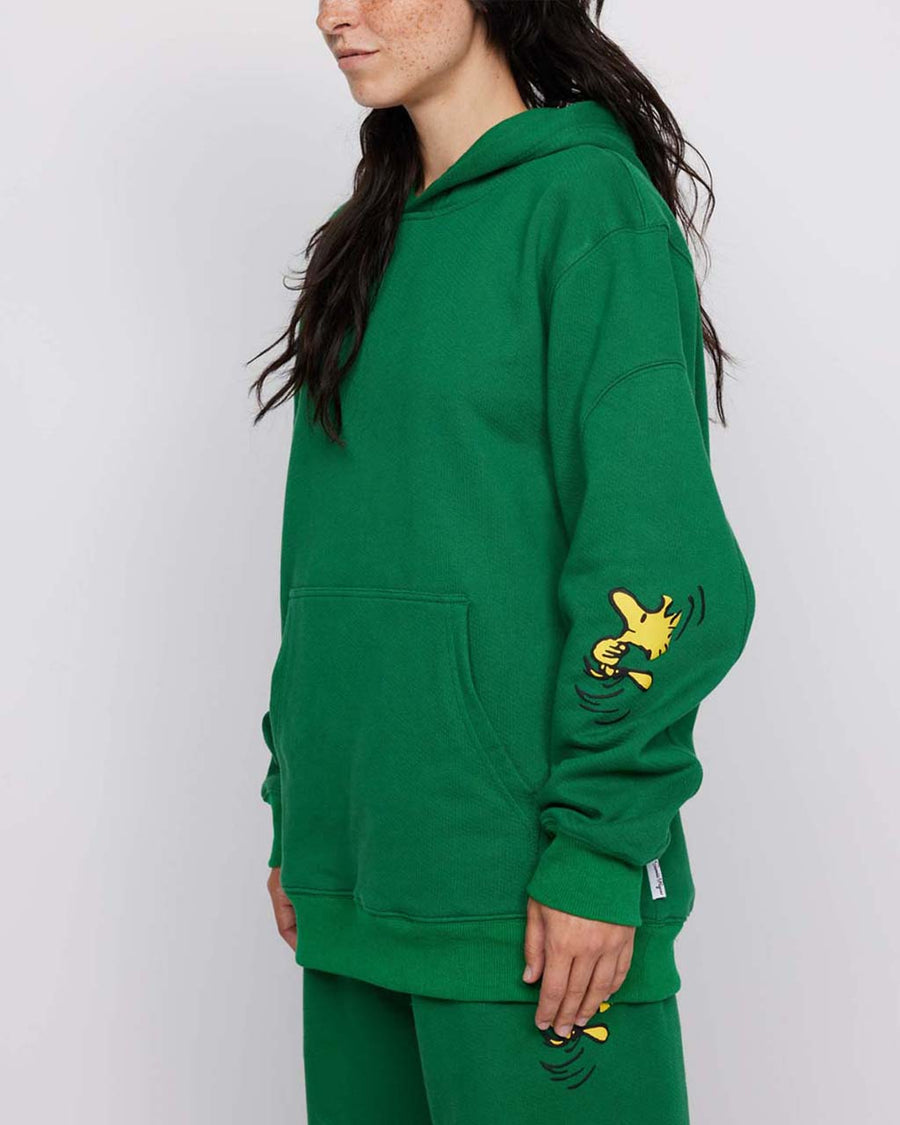 side view of model wearing kelly green hoodie with woodstock and snoopy print on sleeves