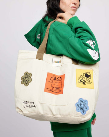 model wearing tan tote bag with various peanuts inspired patches and brown canvas straps