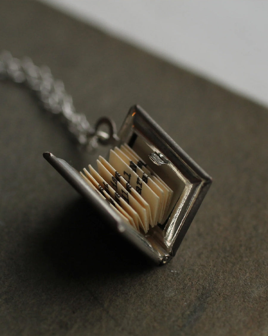 silver book shaped locket with folded paper inside